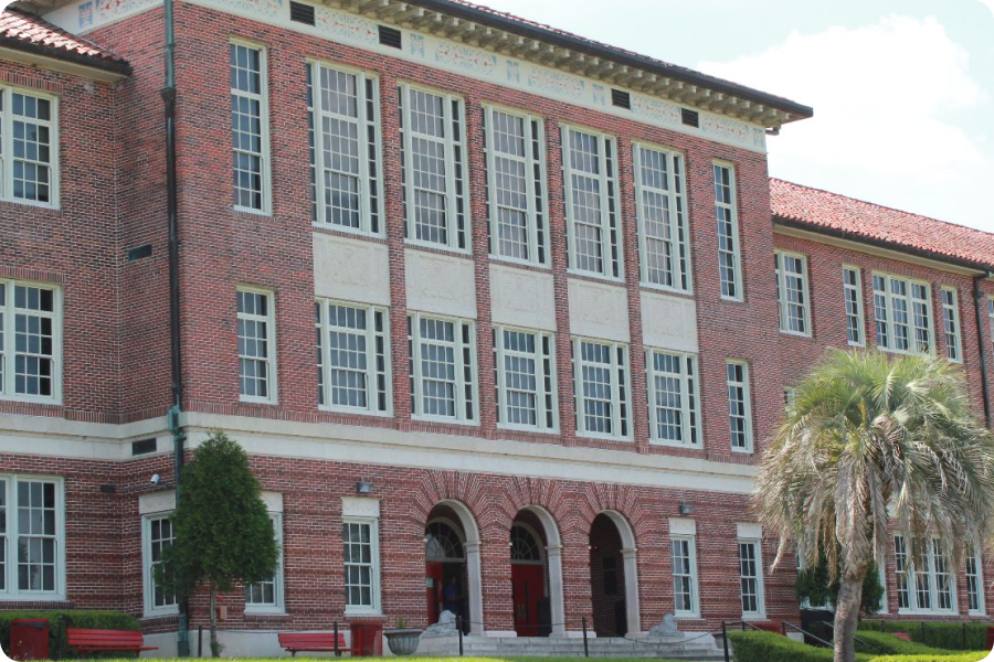 front of red brick building with a palm tree in front